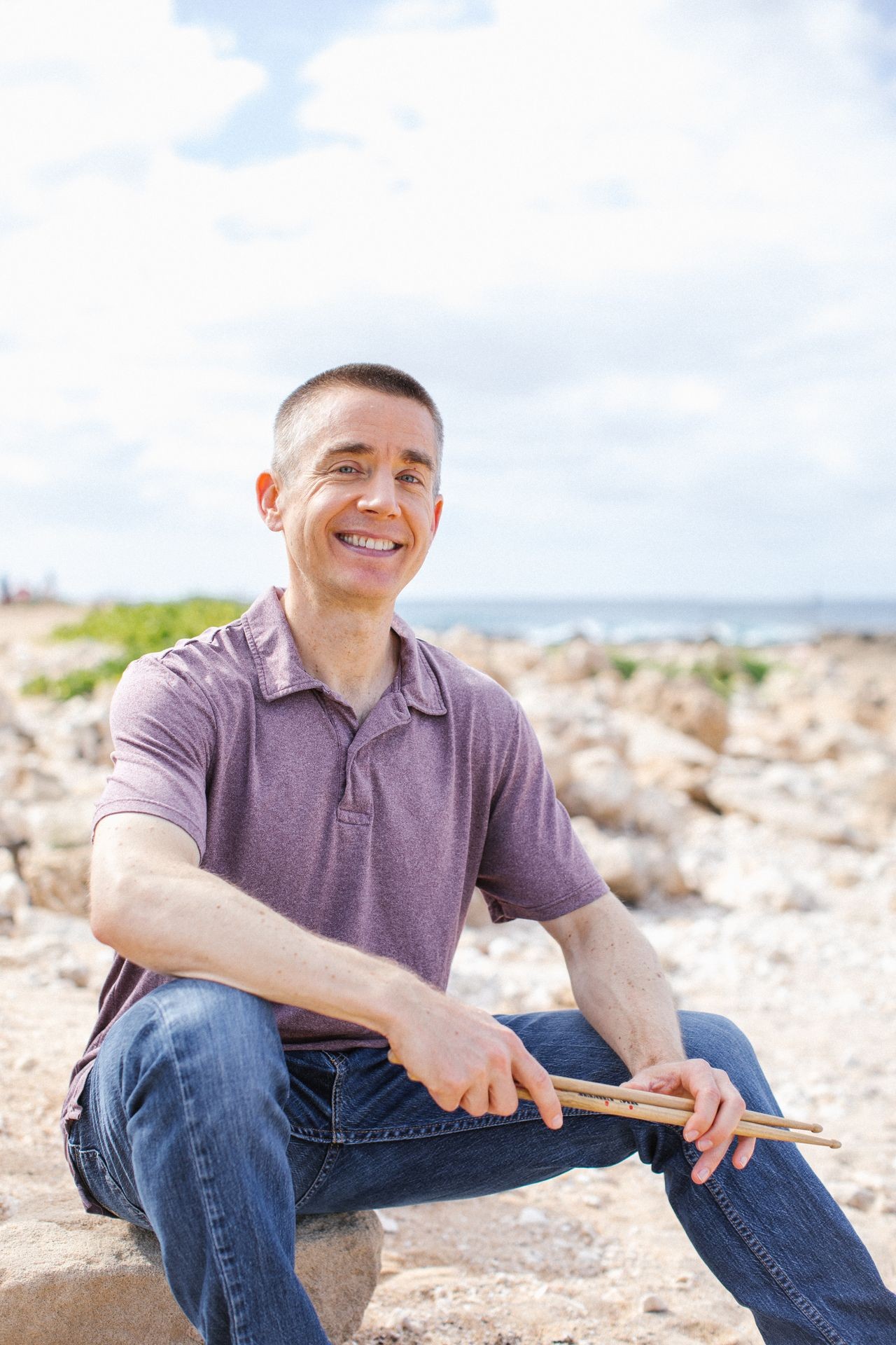 Allan Ward sitting outside smiling, holding drum sticks